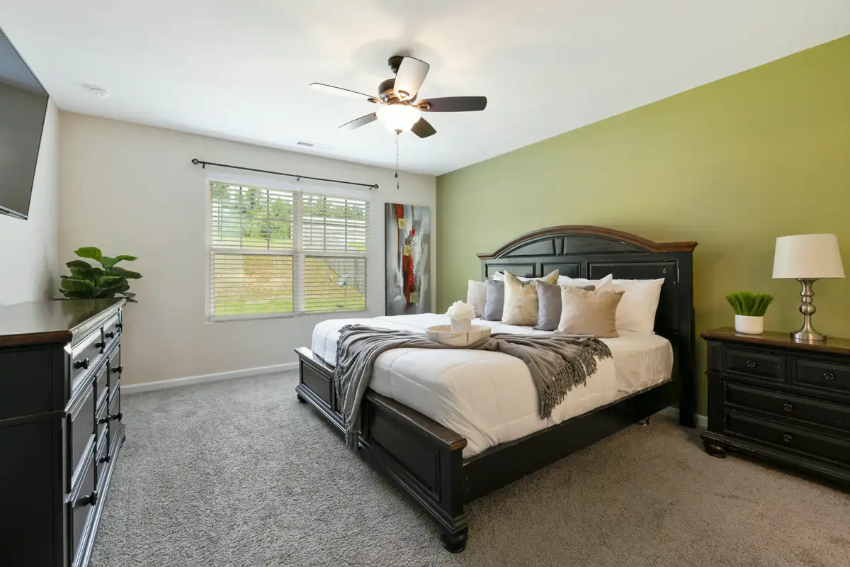 A primary bedroom with a dark wood bed, white bedding, matching nightstands and lamps, a sage accent wall and a ceiling fan.