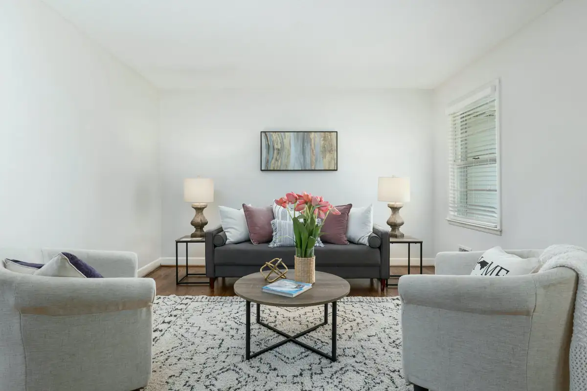 A bright sitting room staged with a grey sofa, two white armchairs, fresh tulips on the coffee table and a framed print above.