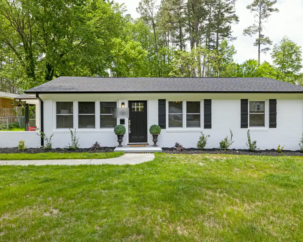 A single-story white brick ranch house with black shutters, a black front door and a wide green lawn.